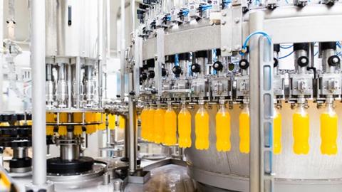 A bottling machine fills plastic bottles with yellow liquid.