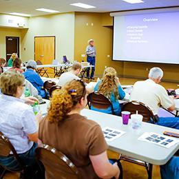 Attendees listen to a presentation by a member of the Forage-Livestock Group in a conference room.