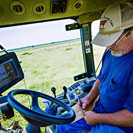 A man takes notes while measuring forage density from the cab of a harvester in a field.