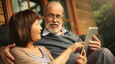 A couple sits on a porch looking at a tablet.