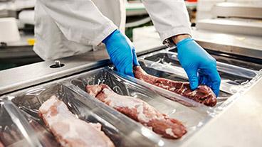 Employee in meat processing facility packaging meat.