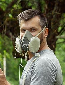 Man wearing a respirator while spraying trees.