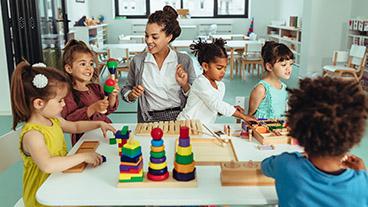 Teacher and young kids playing with toys in childcare setting.