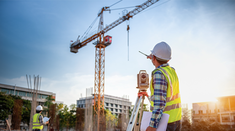 Building site with crane and individual with hardhat pointing to crane.