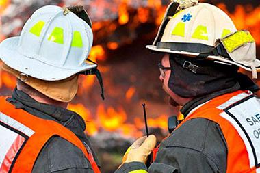 Two firemen standing in front of a fire.