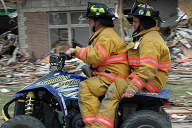 Two firefighters on a four-wheeler driving through rubble.