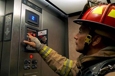 A fire fighter in an elevator working on the emergency call pad.