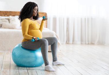 Pregnant woman lifting weights on an exercise ball