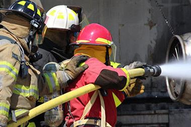 Firefighters pointing a water hose at an aircraft engine.
