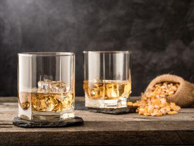 Two tumbler glasses filled with Whiskey and a bag of dried corn
