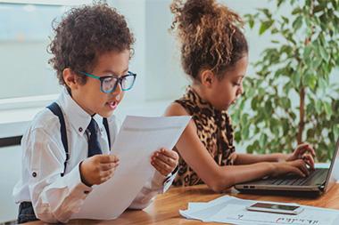 A boy reading a report and a girl typing on a laptop.