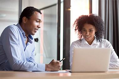Man and woman sitting at table in conference room looking at a laptop together.