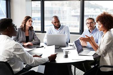 Woman speaking to group of co-workers sitting at office conference table.