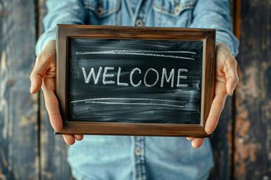 Person holding small "Welcome" sign