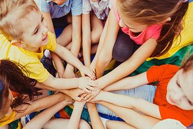 Group of children putting their hands together in the middle of a circle