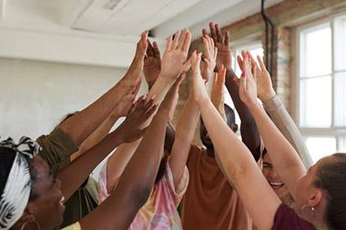 Group of adults gathered in a circle clapping their raised hands together.