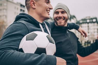 Two men walking onto a track with a soccer ball.