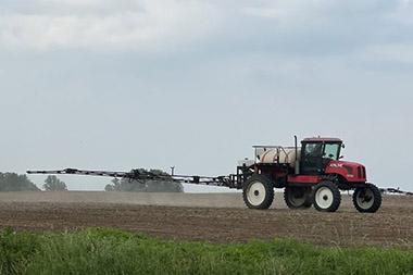 Spray rig attached to tractor spraying a field