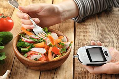 A person with a fork, bowl of vegetables and a blood sugar monitor.