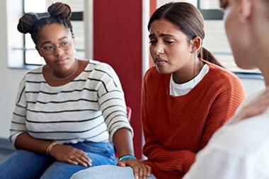 A woman comforting another crying woman in a group session.