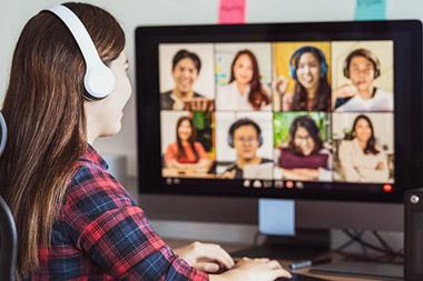 Woman sitting in front of computer screen showing many attendees in virtual meeting