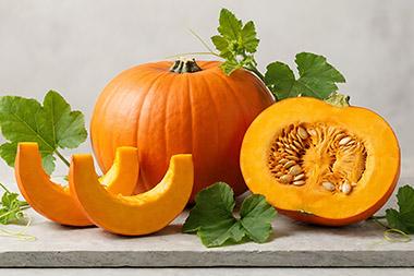 A whole pumpkin, a cut pumpkin and 2 slices of pumpkin sitting on a cutting board.