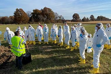 People in hazmat suits standing in a field.