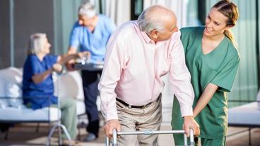 Nusing helping senior man with walker.