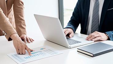 People pointing to paper report and using laptop