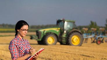 Woman in front of field and harvesting equipment