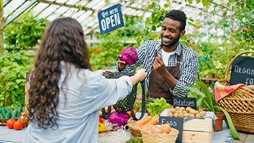 Man selling produce to woman in a greenhouse market