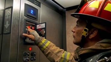 A fire fighter in an elevator working on the emergency call pad.