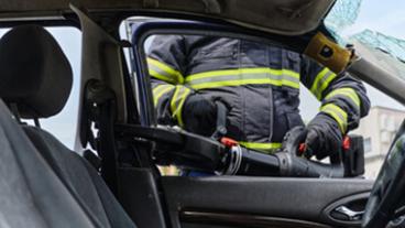 A firefighter cutting a door off a car.
