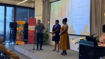 A man speaking on a stage into a microphone with two women standing by him.