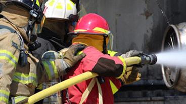 Firefighters pointing a water hose at an aircraft engine.