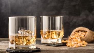 Two tumbler glasses filled with Whiskey and a bag of dried corn