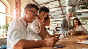 People at an office table looking through documents, computers, and tablets