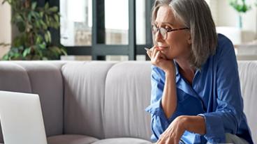 A woman sitting on a couch looking at a computer.