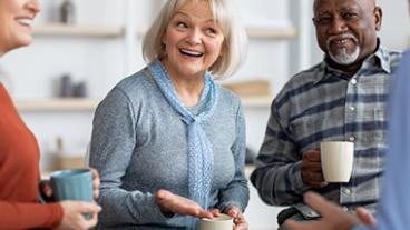 A group of seniors laughing while drinking coffee.