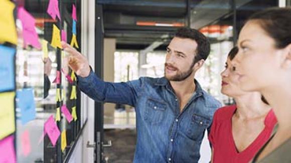 Businesspeople looking at a board covered with sticky notes.