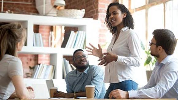 Black female speaking to a diverse group of colleagues.