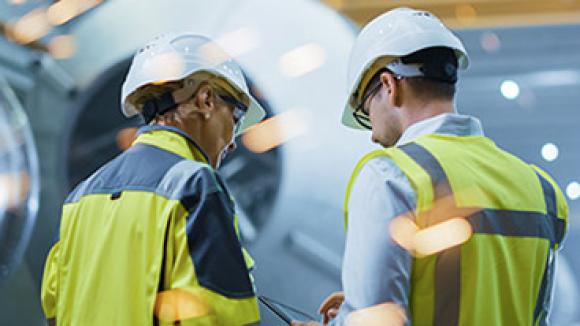 A man and woman in a factory wearing hard hats.