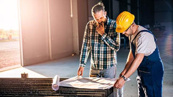 Two construction workers overlooking plans.