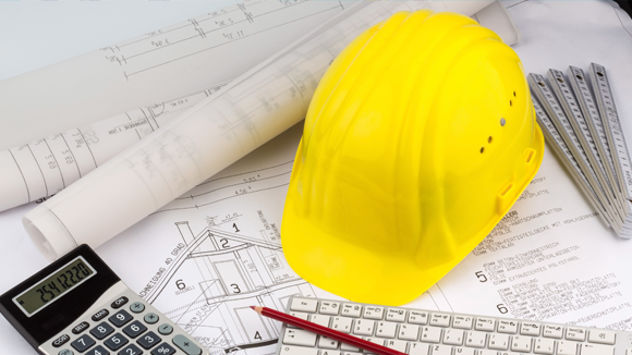 hard hat surrounded by keyboard, calculator and house plans