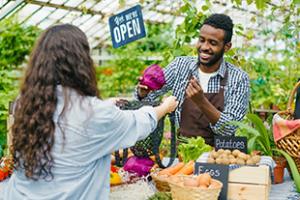 Man selling produce to woman in a greenhouse market