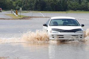 A car driving through flood waters on a road.