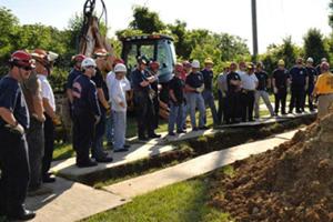 A group wearing hard hats standing over a trench.