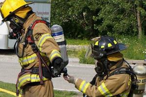 A fire fighter checking oxygen levels in a tank for another fire fighter.