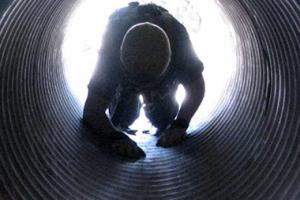 A rescue worker crawling through a drainage pipe.