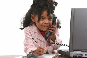 Young girl wearing pink blazer on phone in front of laptop pretending to be working